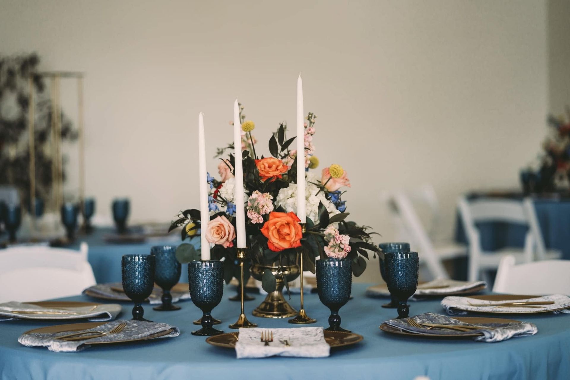Elegant banquet table with blue tableware and a floral centerpiece featuring orange and white flowers.