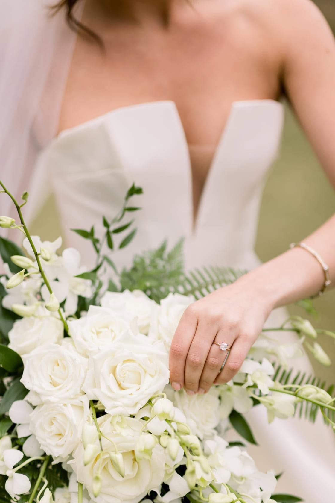 Bride in a strapless white dress holding a bouquet of white roses and greenery