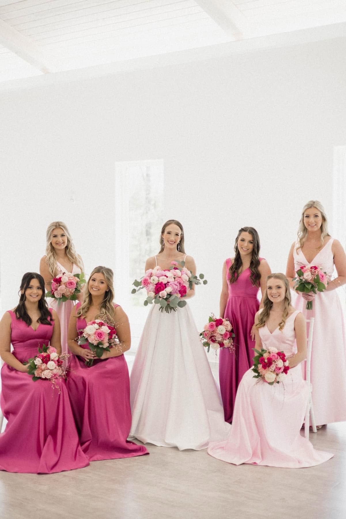 Bridal party in pink and white dresses posing with bouquets in a bright white studio