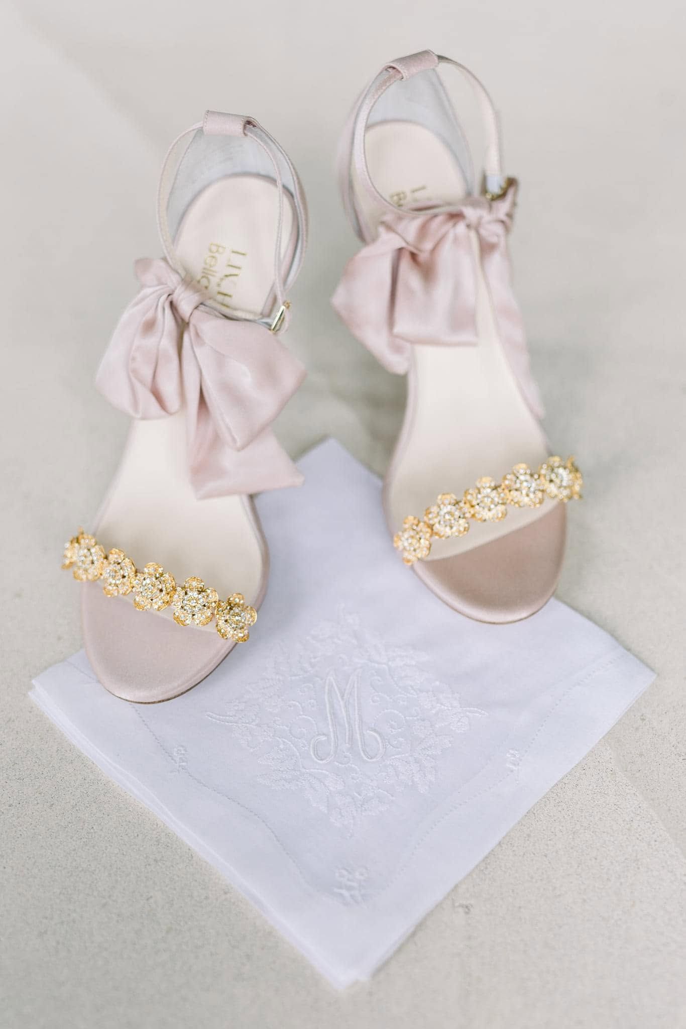 Pair of pale pink jeweled sandals with bows on a white cloth background