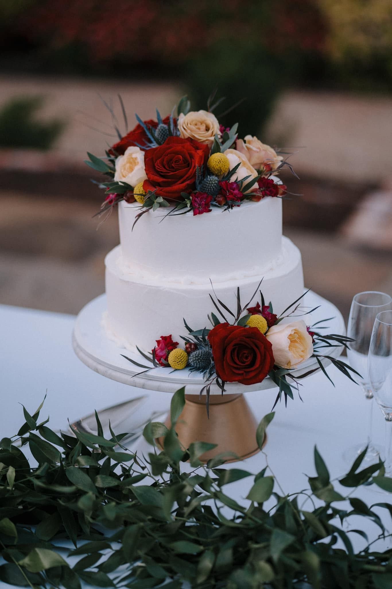 Two-tier white wedding cake with red and peach floral decorations on a decorated table