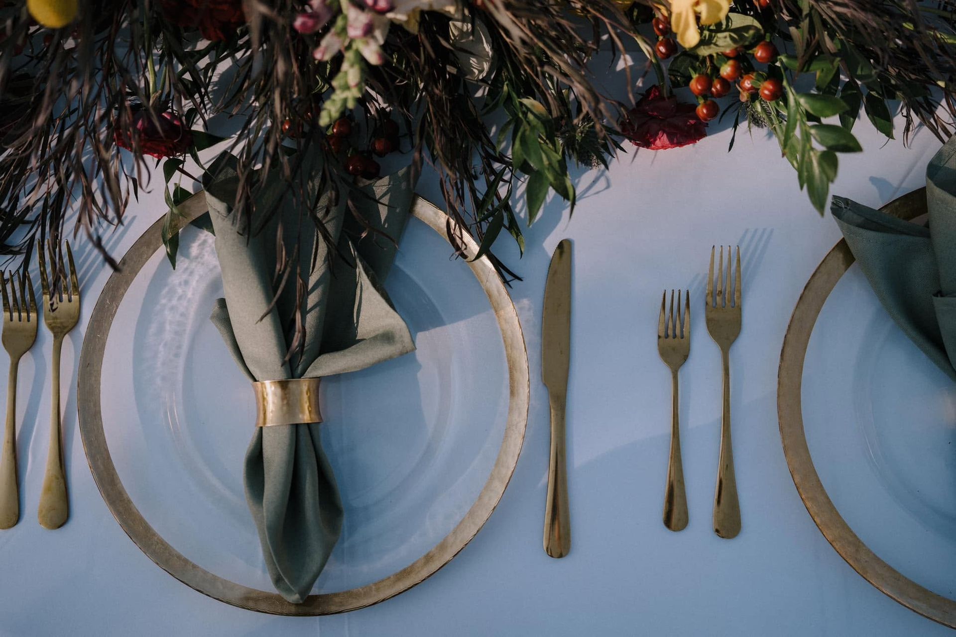 Elegant table setting with gold-rimmed plates, napkins, and cutlery under a floral centerpiece