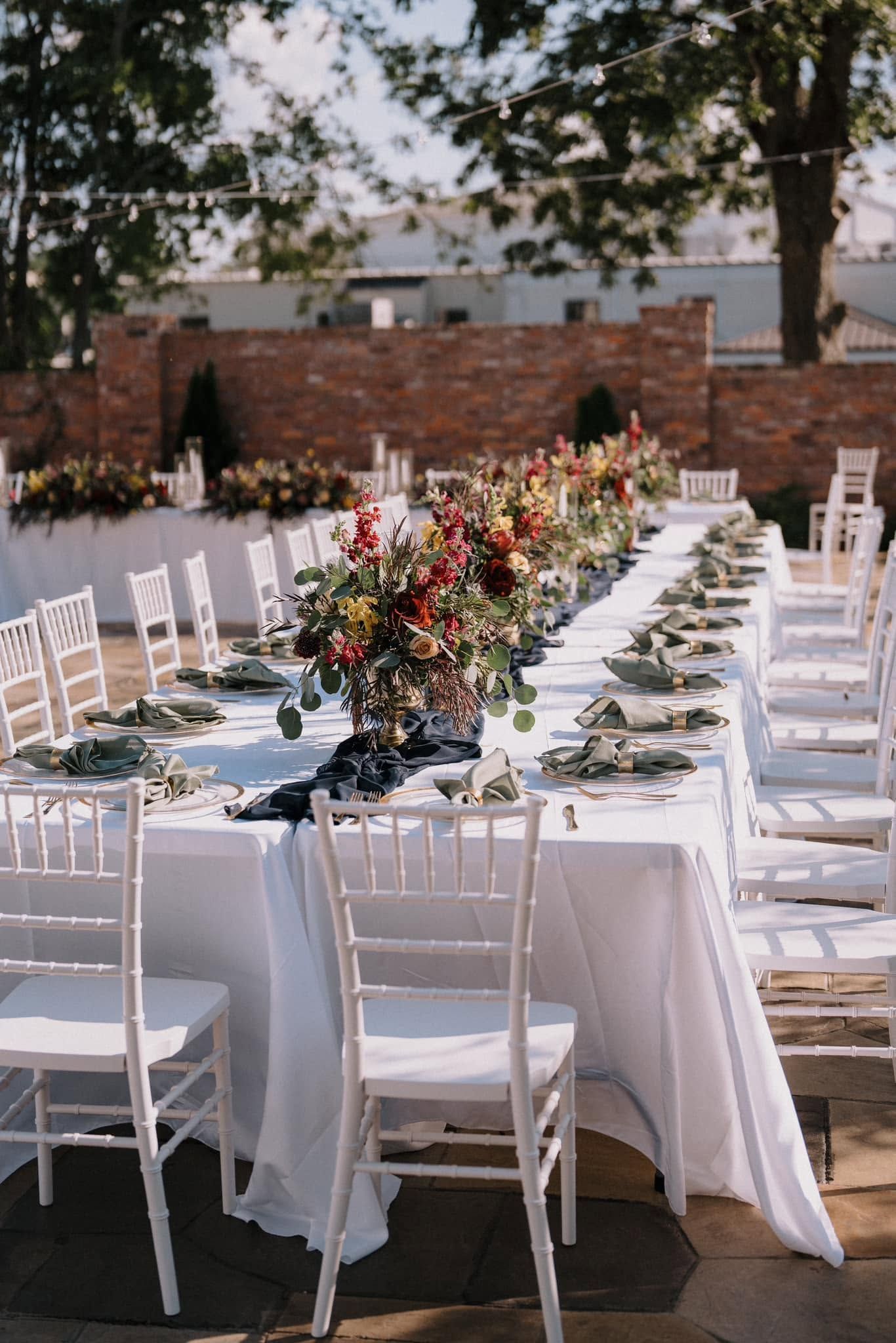 Outdoor dining table set with white chairs and floral centerpiece in a garden setting