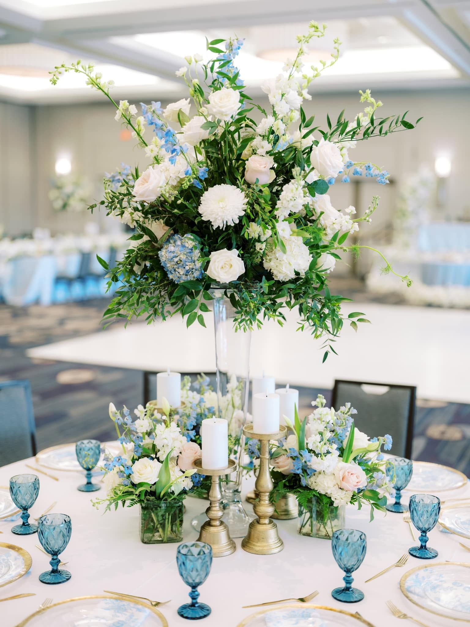 Elegant white and blue floral centerpiece on a banquet table with blue glassware in a bright reception hall