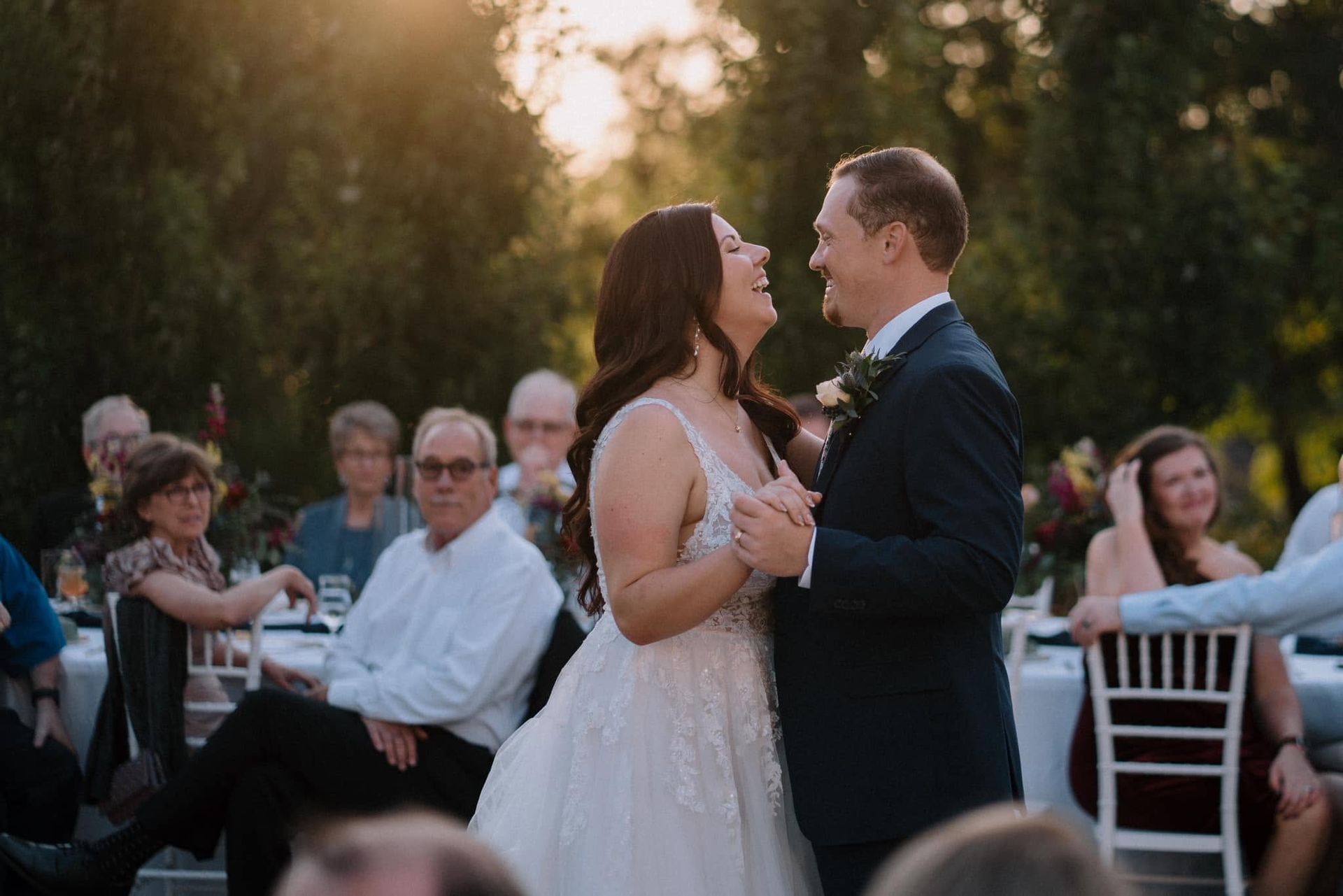 Bride and groom share a dance at an outdoor wedding reception at sunset.