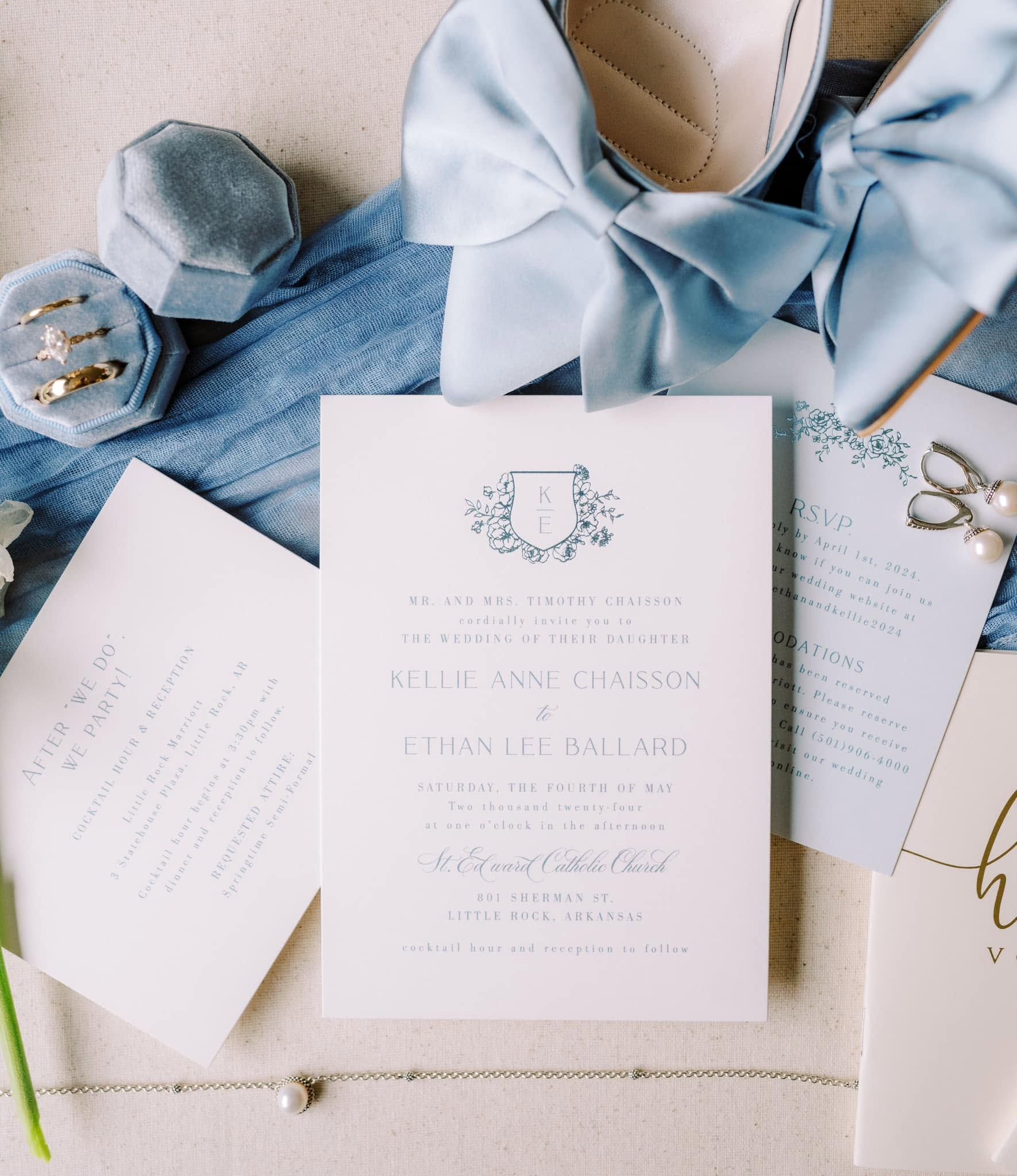 Elegant wedding invitation suite with pale blue ribbon, lace, and perfume on a textured blue-and-white surface
