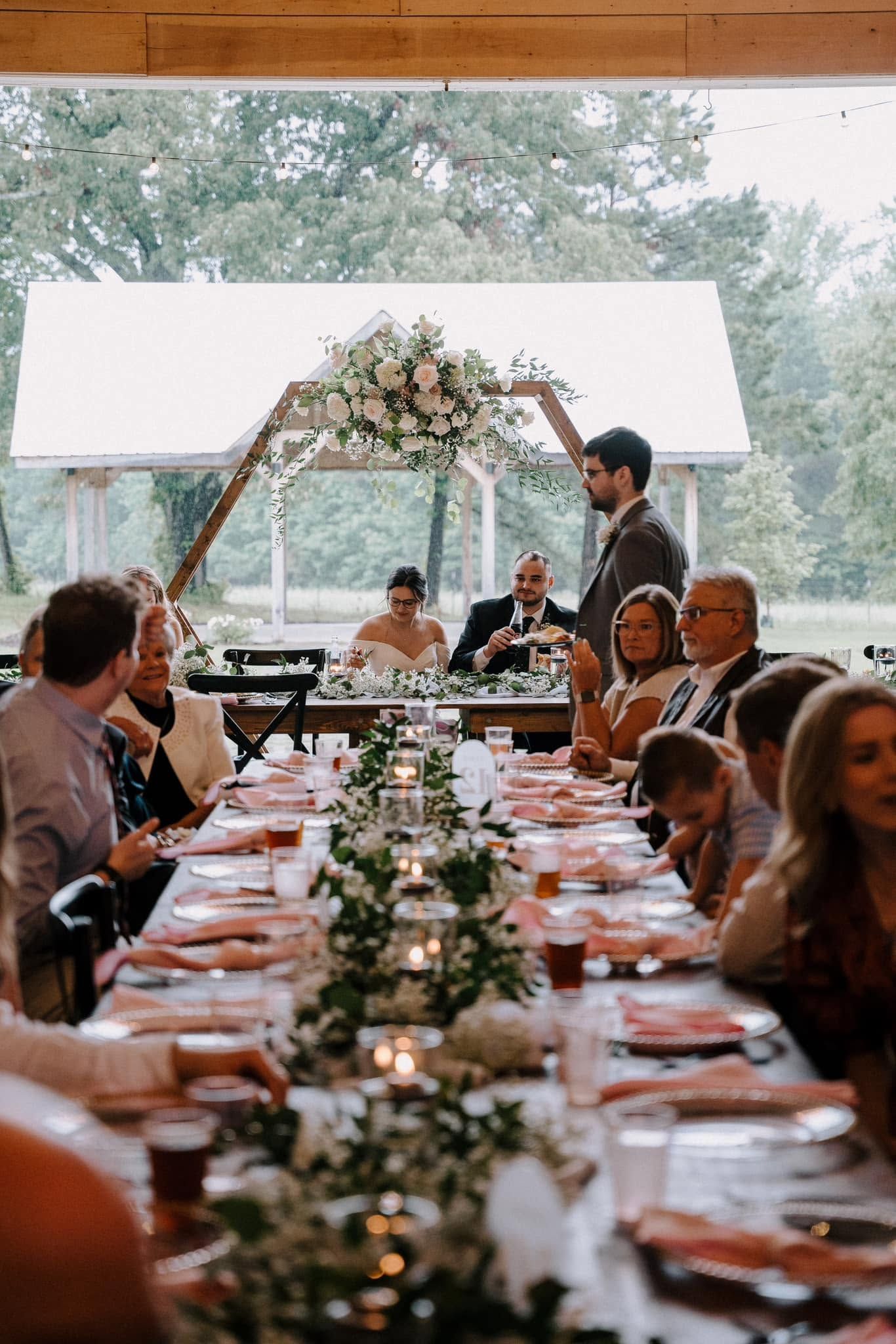 Long banquet table under a floral arch at a rustic indoor-outdoor wedding reception