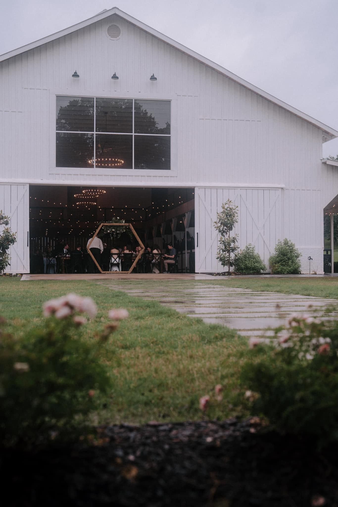 White barn-style house with large open garage and a grassy foreground by a paved path
