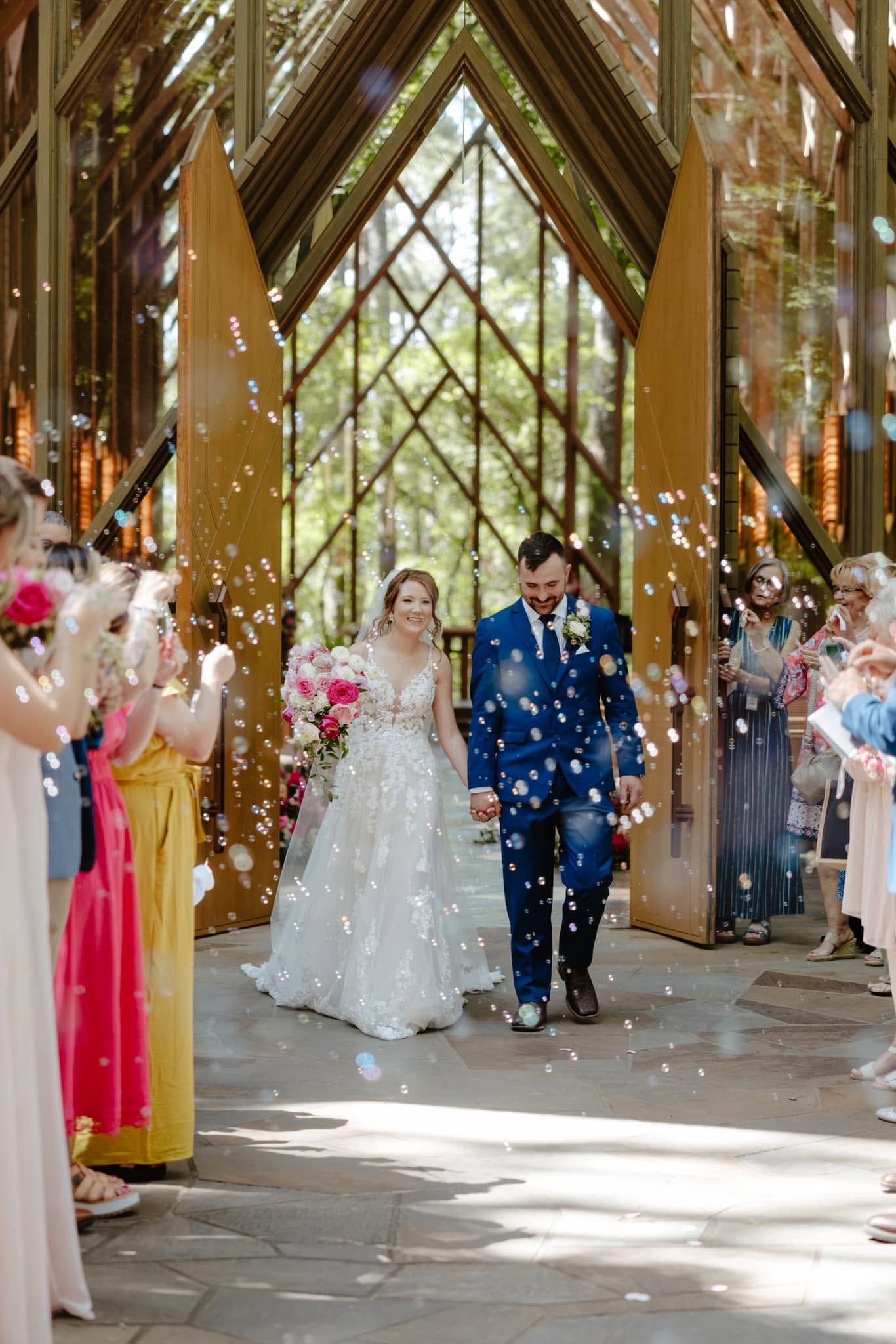 Bride and groom walk through flower petals under a wooden arch at an outdoor wedding ceremony
