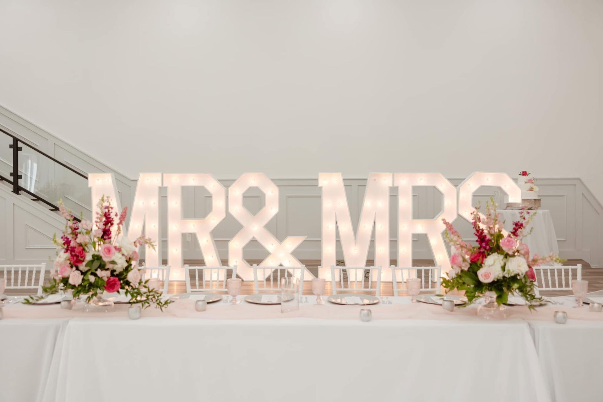 Wedding reception table with pink floral arrangements and illuminated “MR & MRS” sign