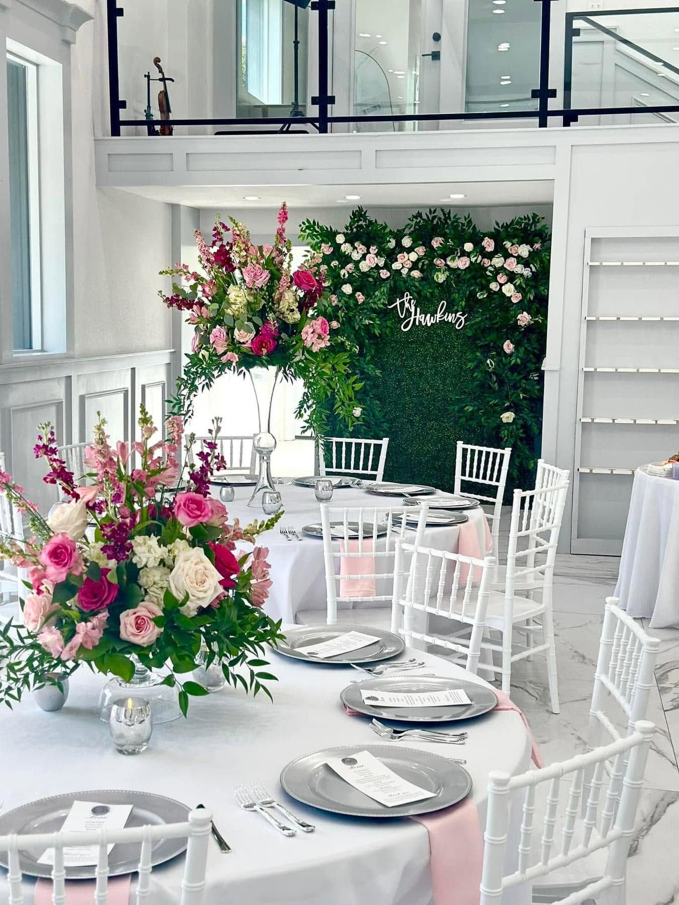 Elegant white dining room with floral arrangements, white chairs, and a green floral wall backdrop