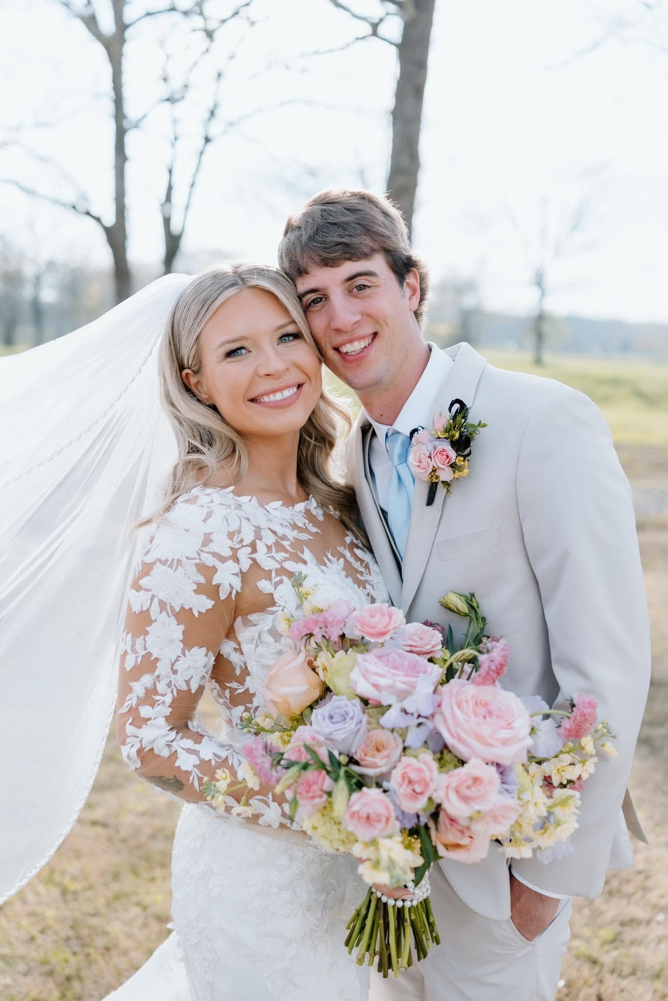 Smiling bride and groom outdoors, holding a pink and white bouquet on their wedding day