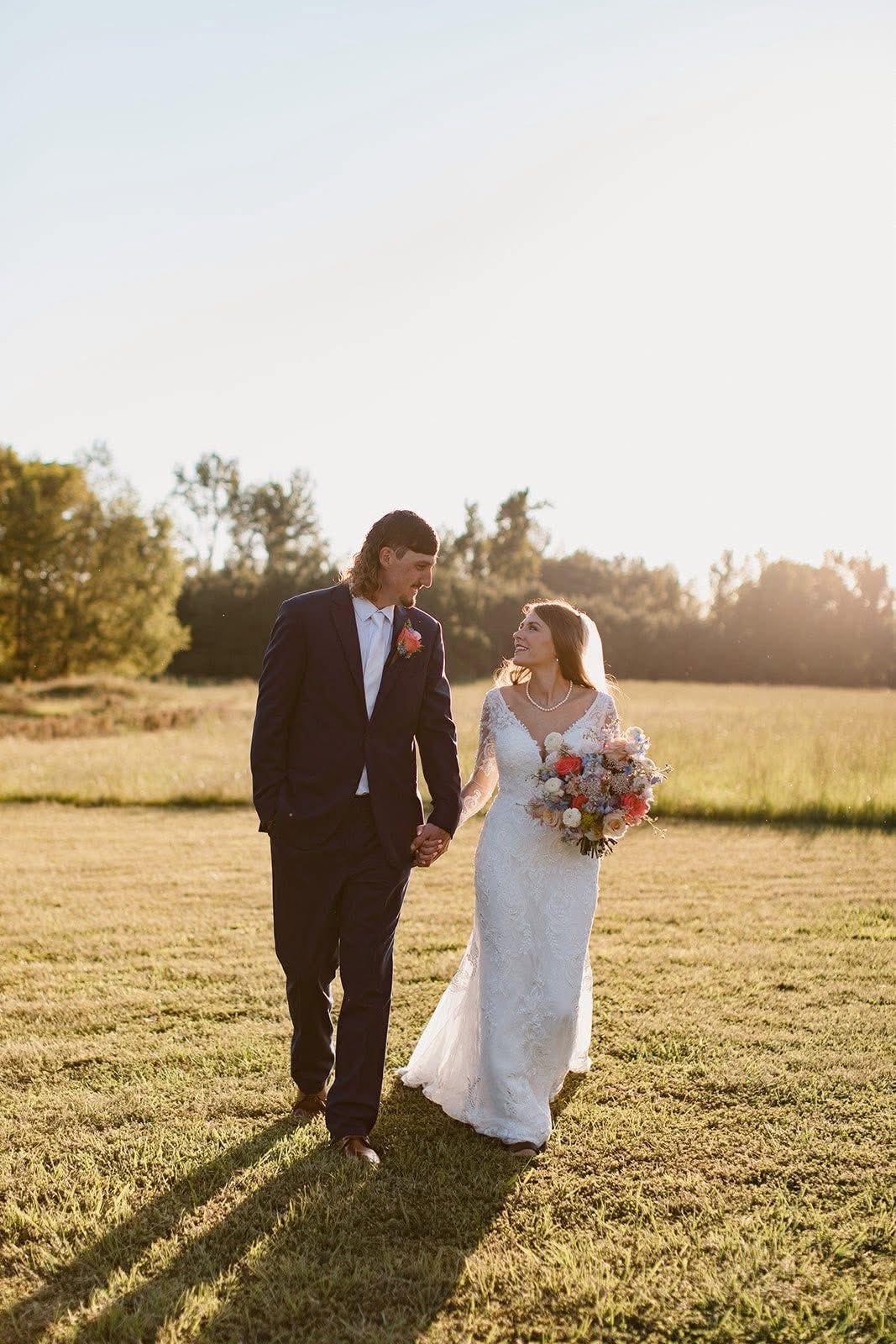 Bride and groom walking hand in hand in a sunny field, bride holding a bouquet