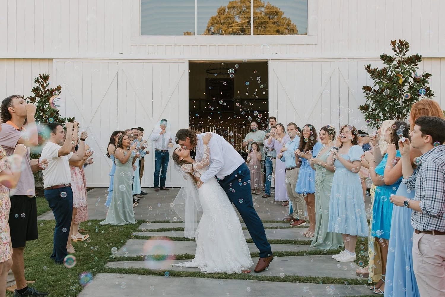 Wedding couple kissing in an outdoor aisle as guests in blue and white cheer and toss confetti