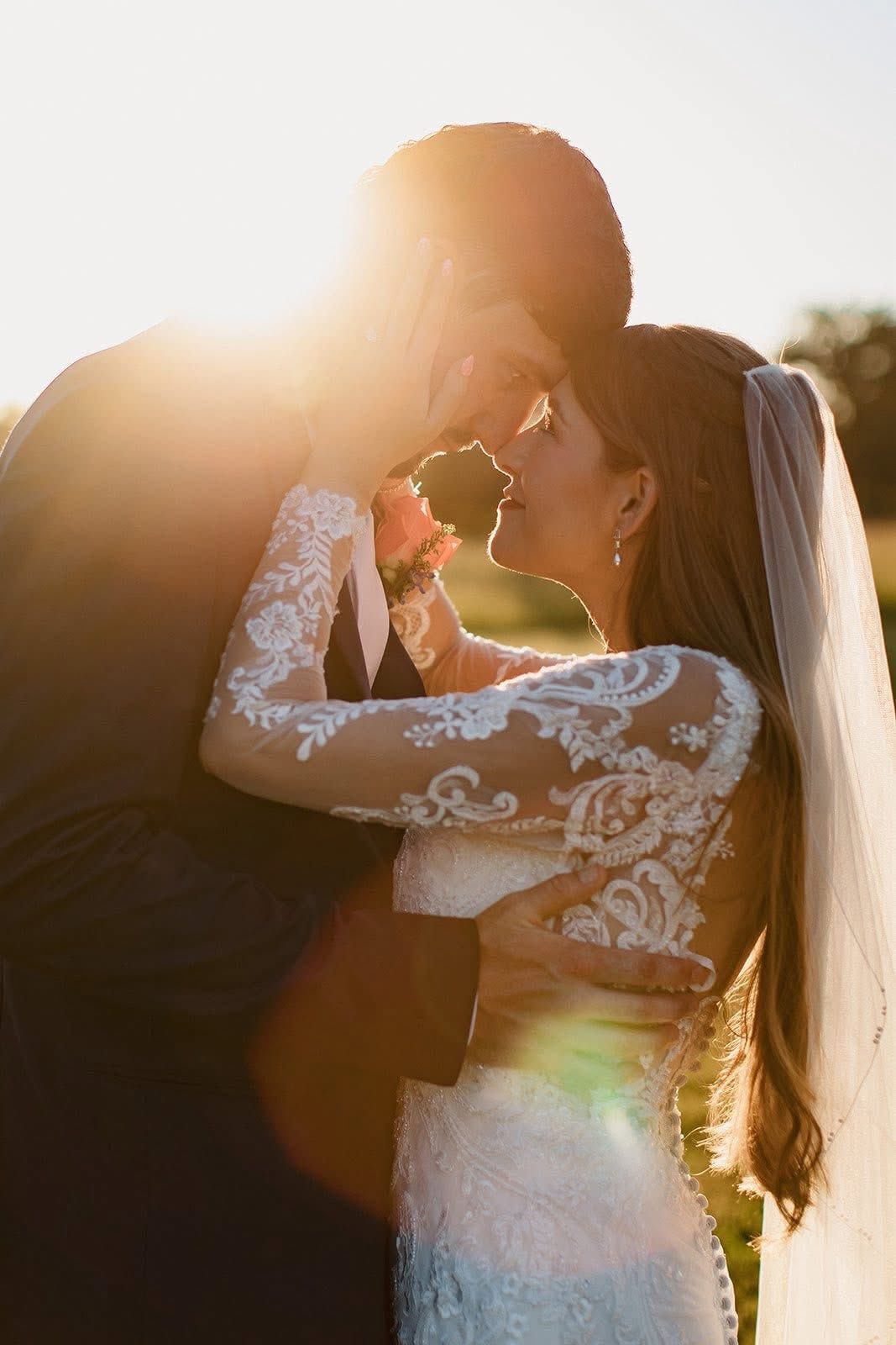 Bride and groom embracing outdoors at sunset, backlit by warm golden sunlight.