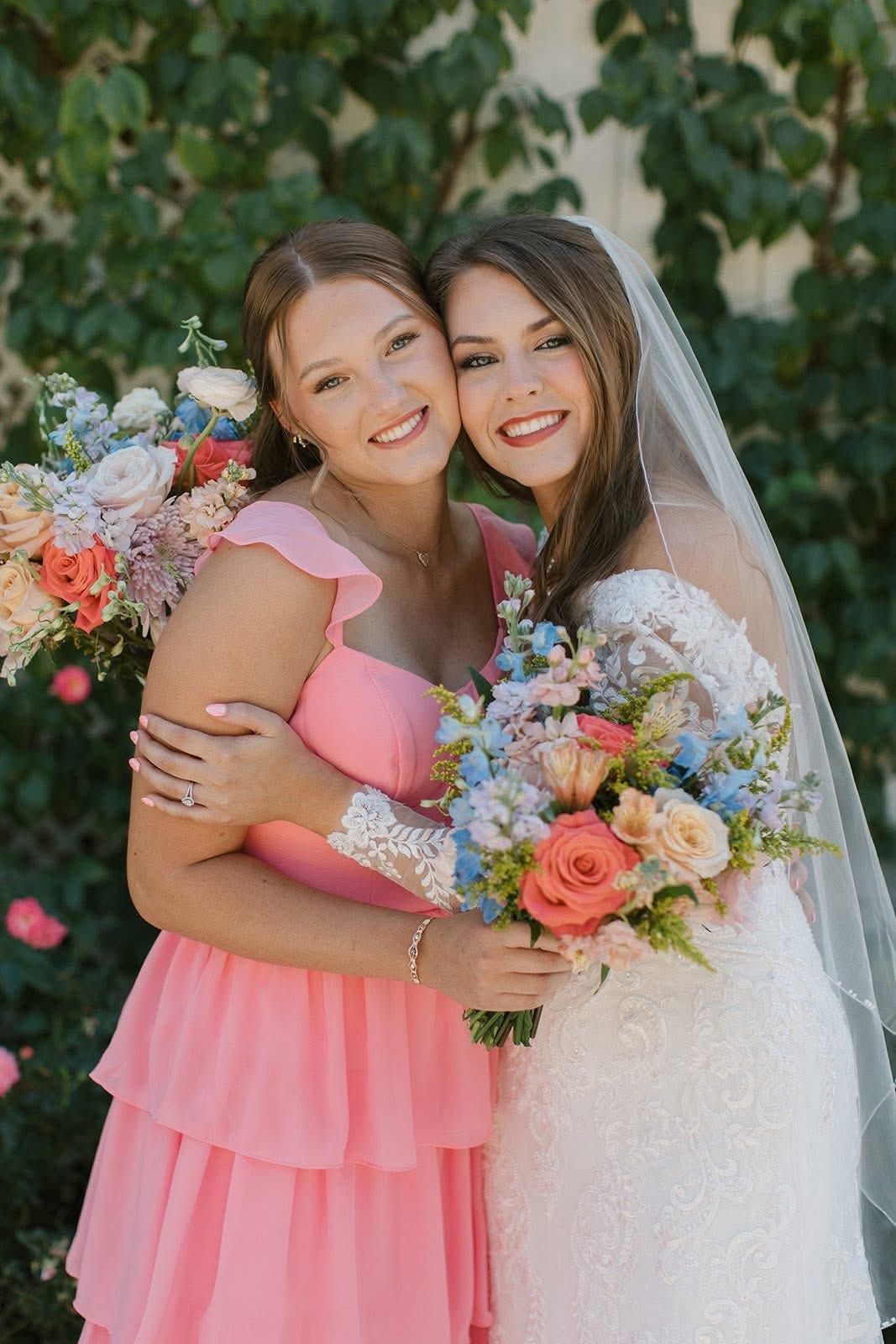 Two women in pink and white dresses smiling and holding bouquets in a garden setting