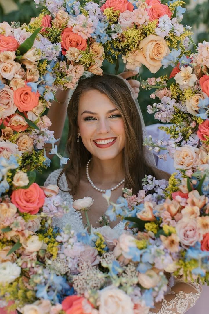 Portrait of a smiling woman framed by a colorful flower wreath, wearing a pearl necklace