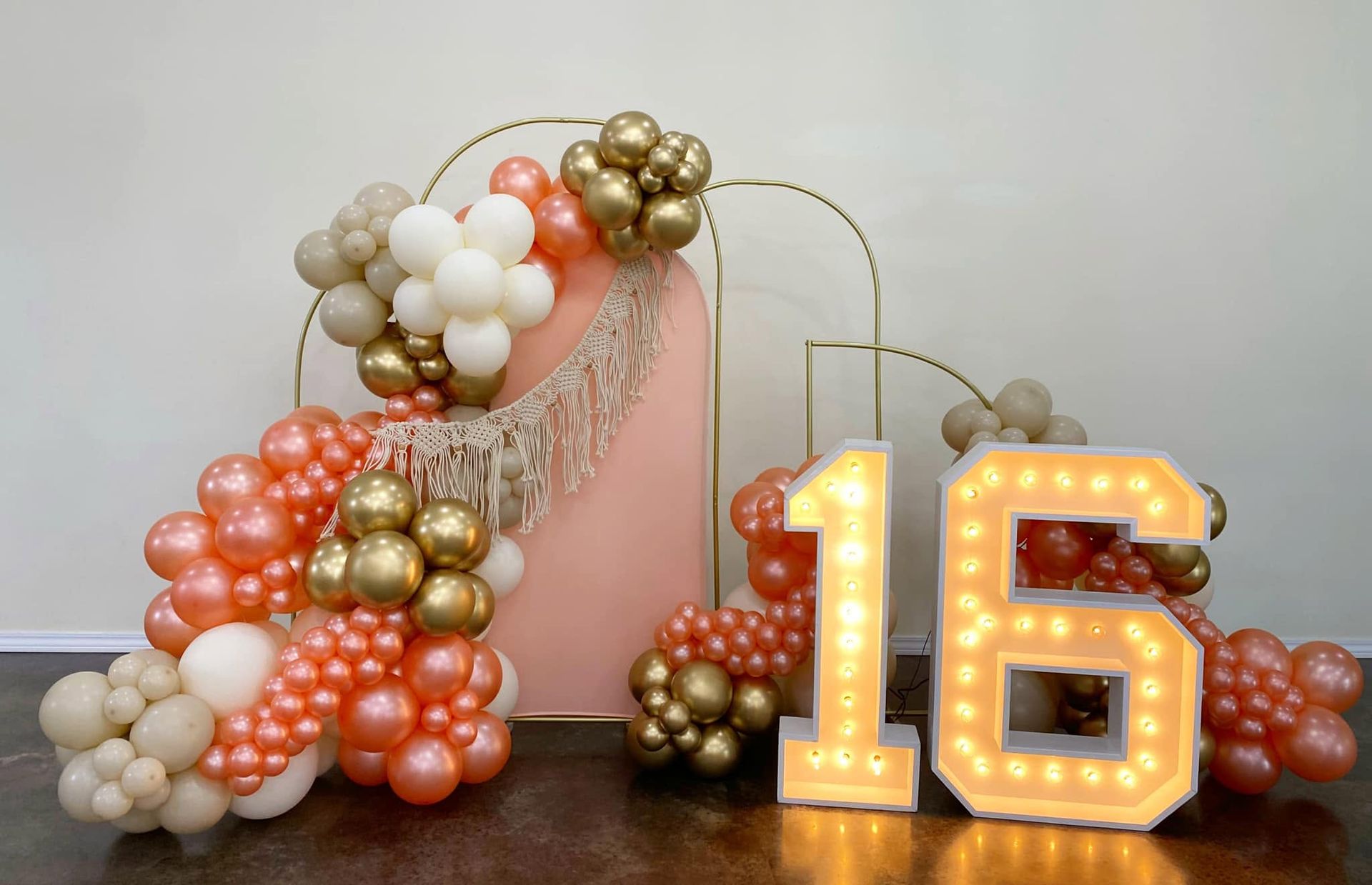 Pink, gold, and white balloon garland with lit “15” marquee numbers on a table