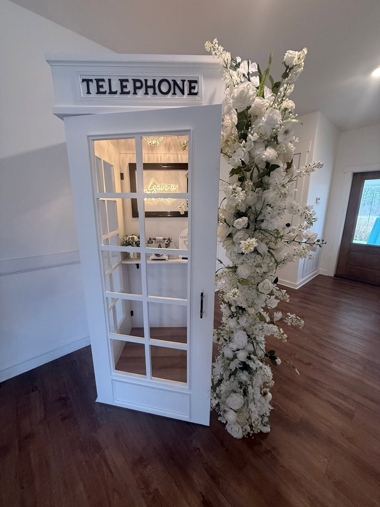 White vintage telephone booth with floral decorations in a room with wooden floors
