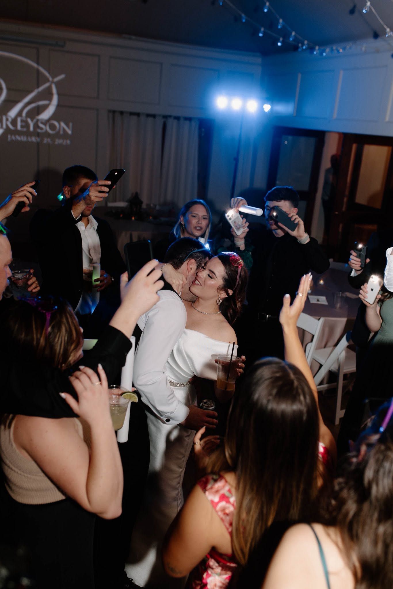 Guests dance and raise phones at a lively party in a dimly lit room with blue stage lights.