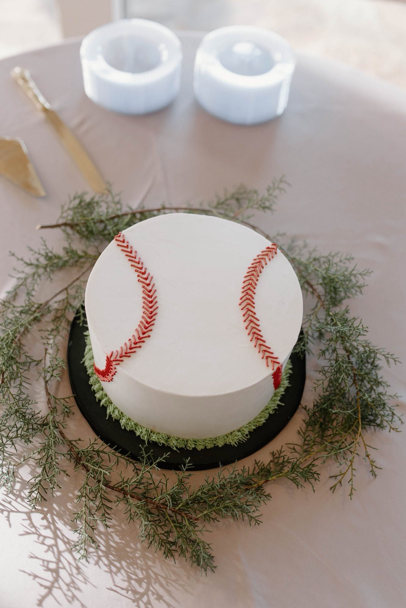 White cylindrical cake with red curved decorations, framed by greenery on a table.