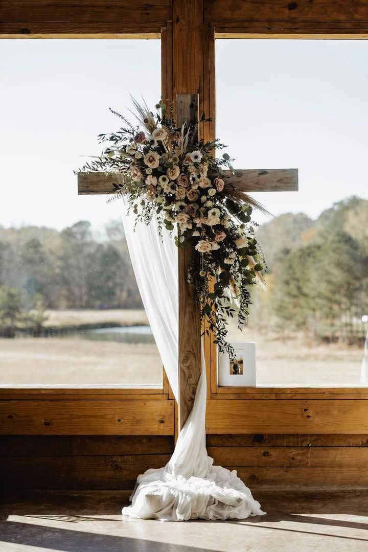 Floral wedding arch with white drape in front of a large window and rustic wooden wall