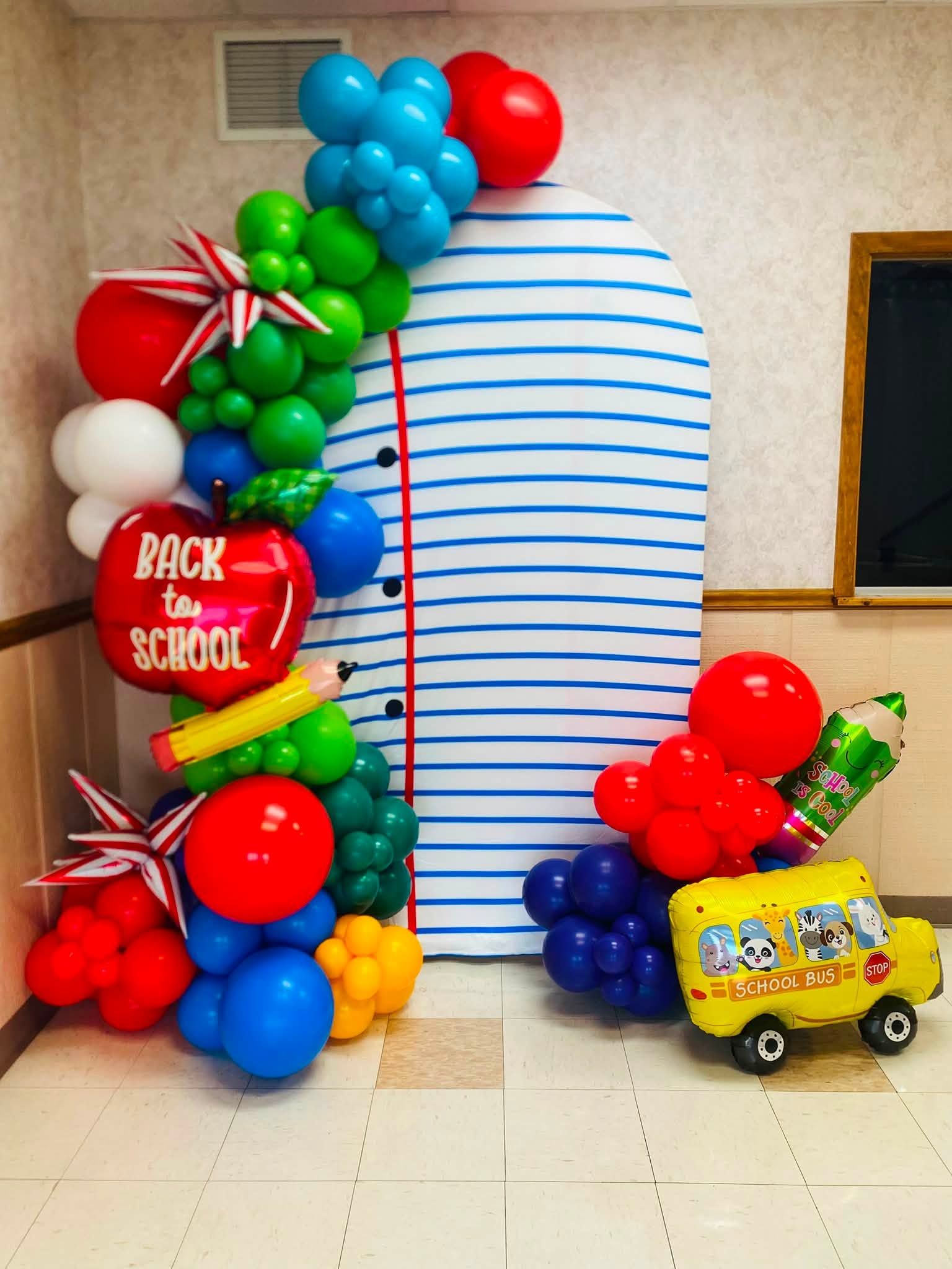 Back-to-school balloon display with blue-and-white backdrop and colorful balloons, plus a school bus toy