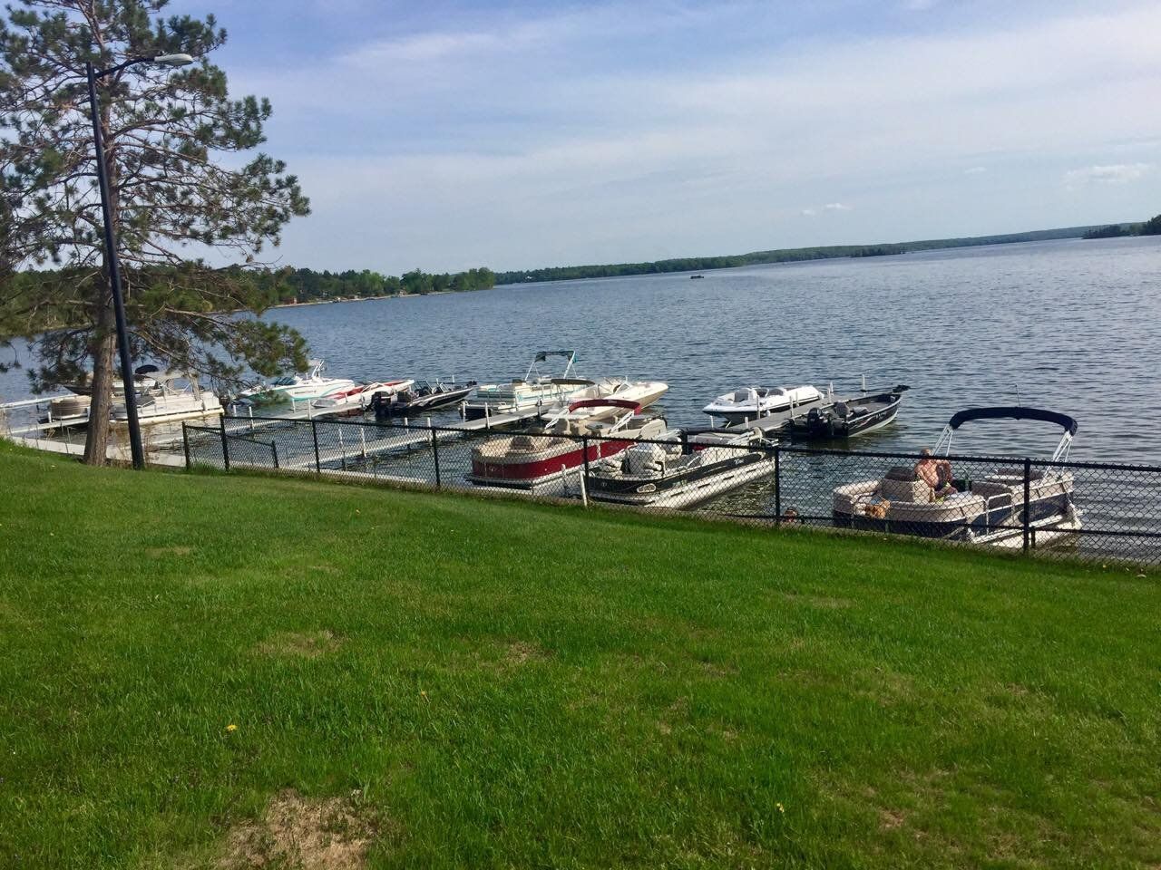 A row of boats are docked at a marina on a lake.