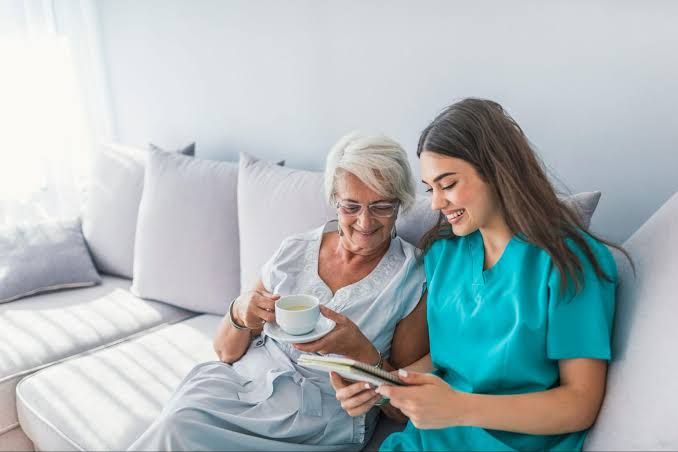 Two people sitting on a couch, smiling and looking at a tablet together while holding cups of tea.