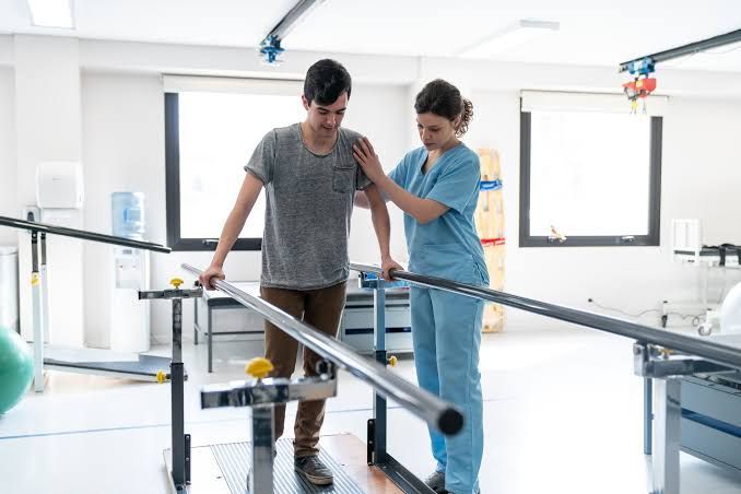 Therapist assisting a patient on parallel bars during physical rehabilitation in a bright clinic