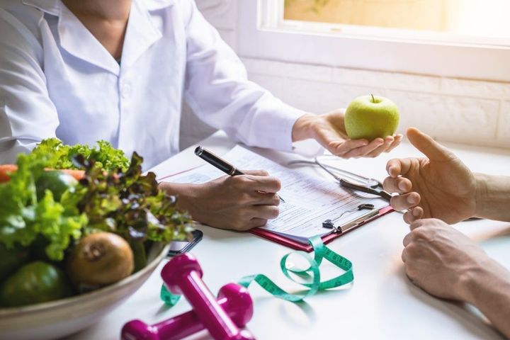 Doctor discussing nutrition with patient over paperwork and green apple on a bright desk