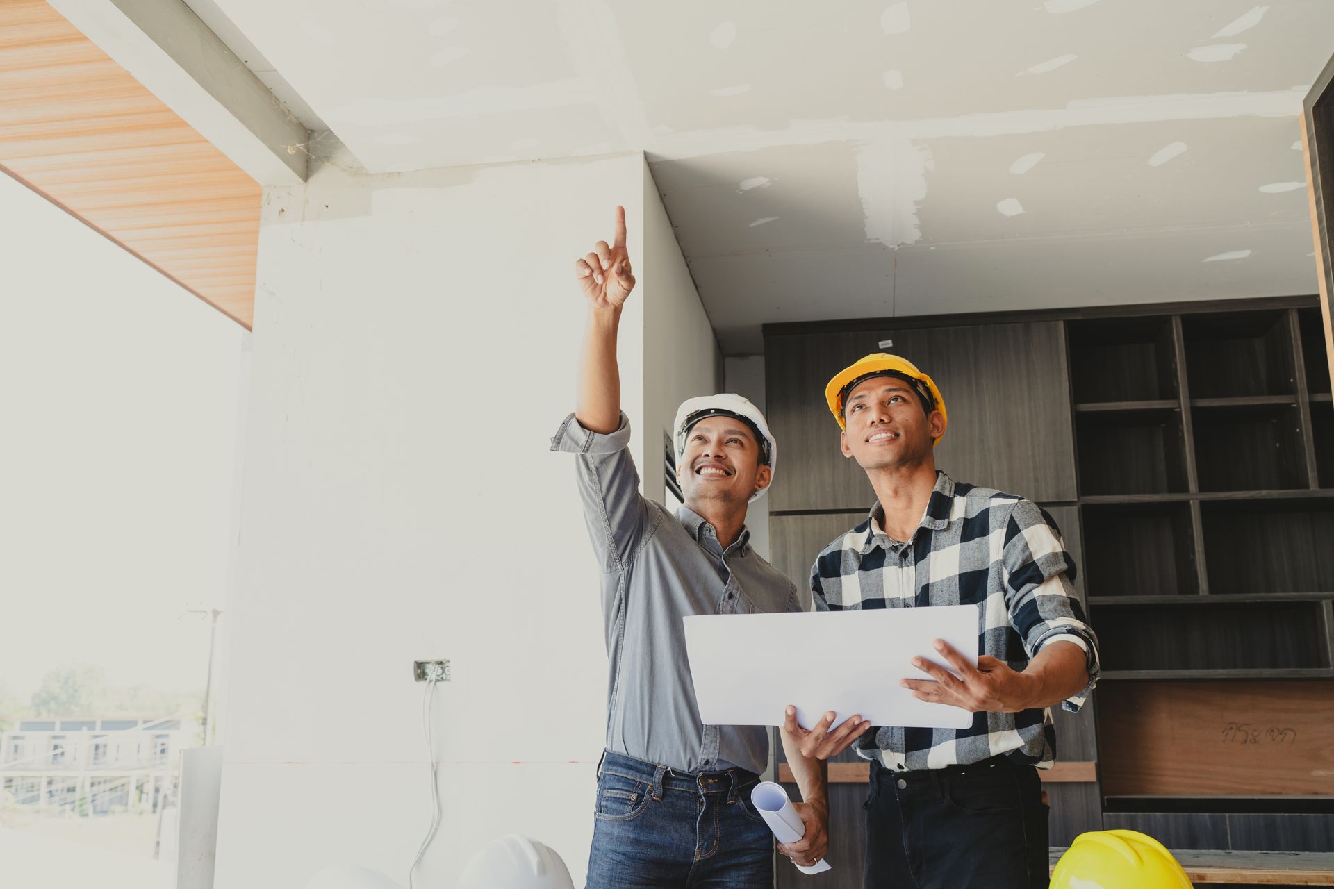 Two construction workers are looking at a blueprint in a room.