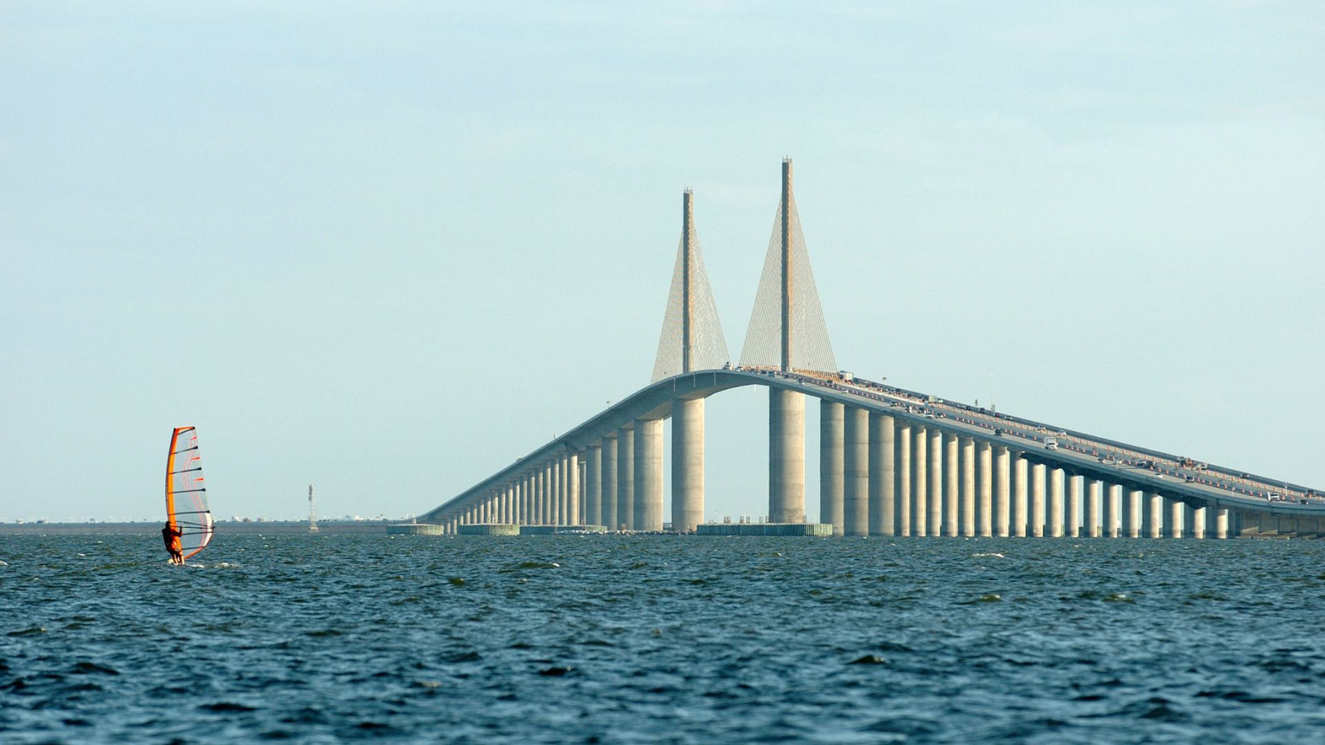 A bridge over a body of water with a sailboat in the foreground.