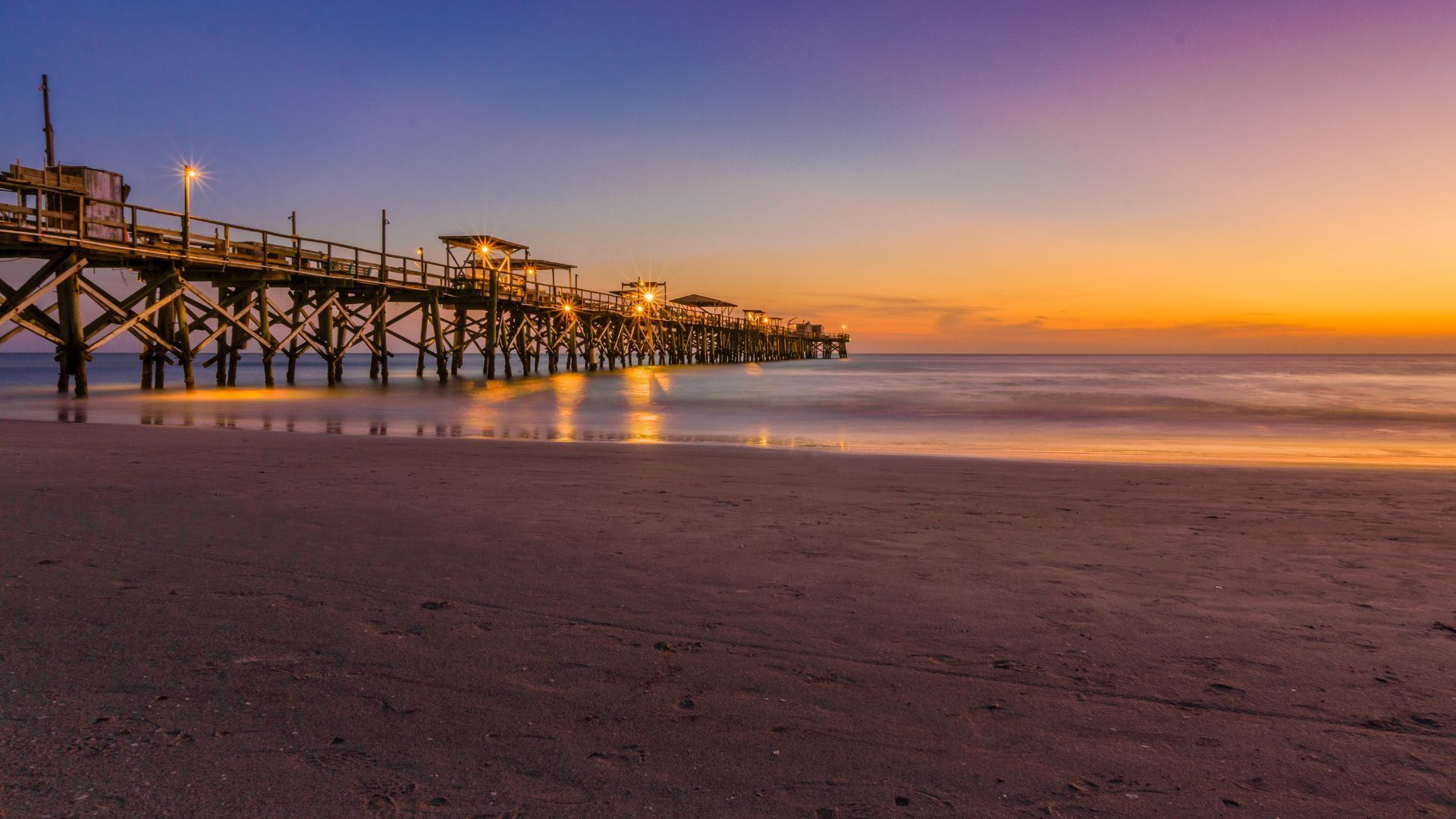 There is a pier on the beach at sunset.