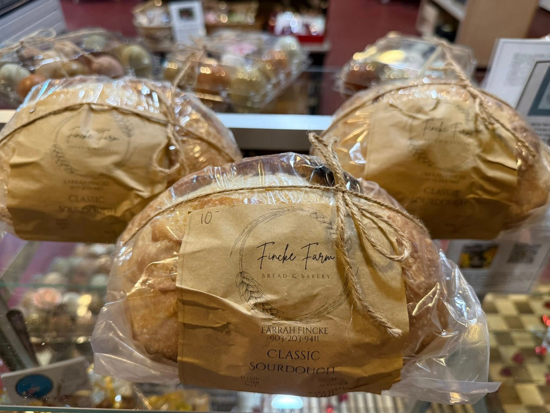 Three loaves of wrapped sourdough bread on display in a bakery.