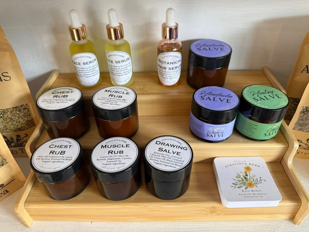 Products displayed on a bamboo shelf: oils, salves, and a card set. Jars have white labels with black text.