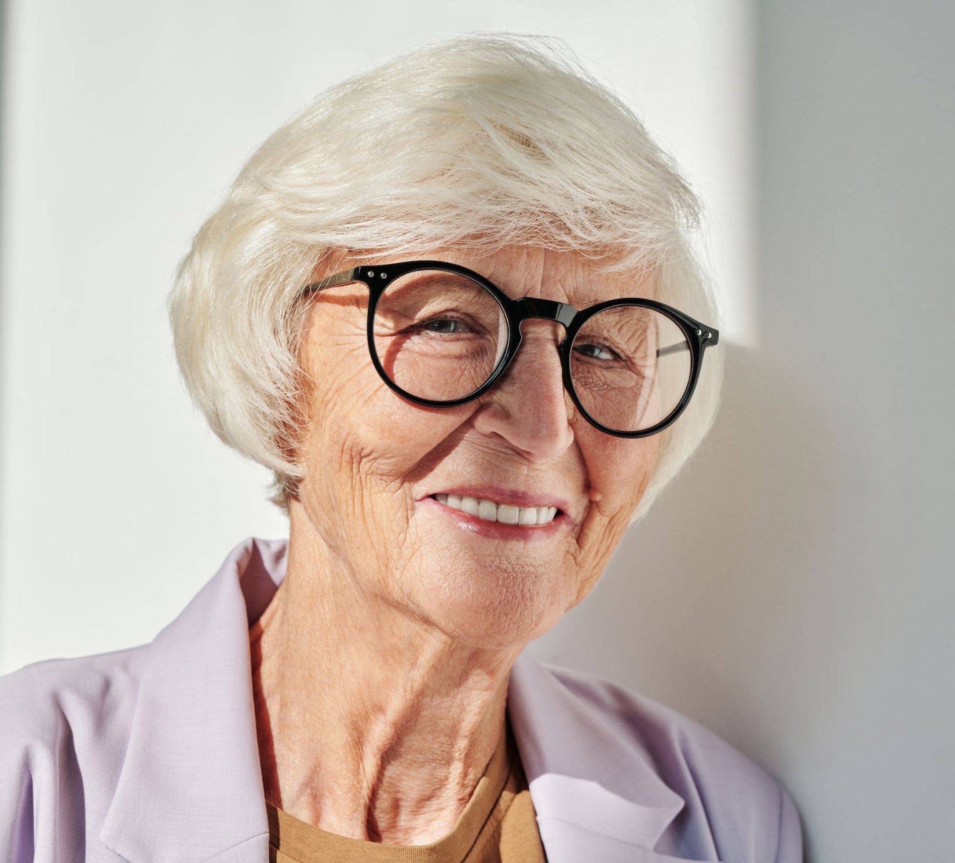 Smiling older woman with white hair and glasses, wearing a lavender blazer.