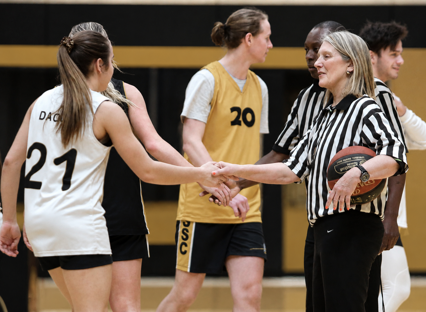 Basketball players and a referee shake hands during a gym court game.