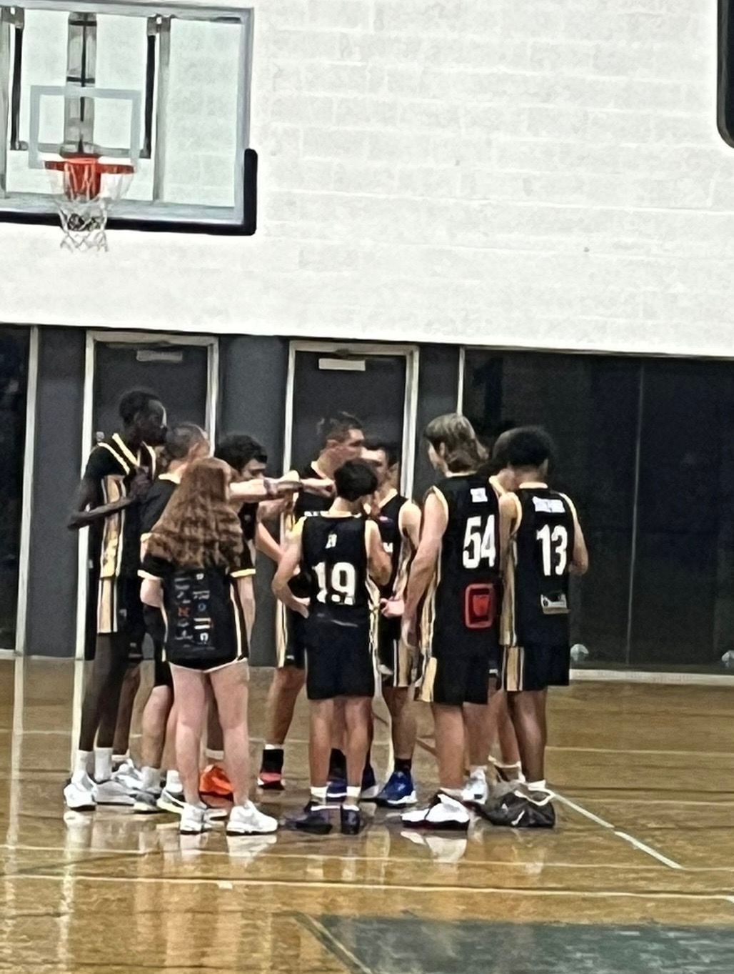 Basketball team in blue uniforms huddles on an indoor court before practice or a game.