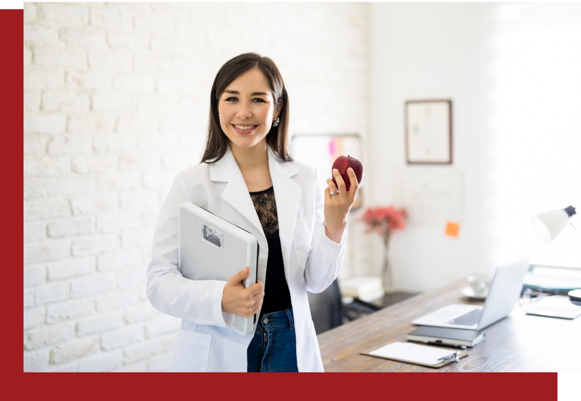 A woman in a lab coat is holding an apple and a laptop.