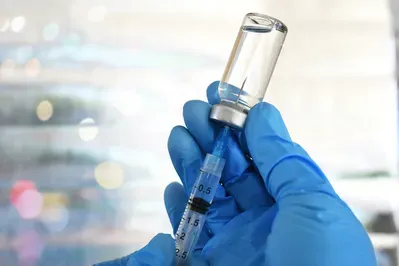 A person wearing blue gloves is holding a syringe and a bottle of vaccine.