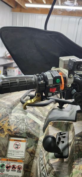 Close-up of ATV handlebars, camo body, black controls.