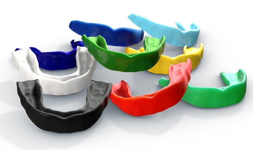 A Group of Mouth Guards of Different Colors Are Sitting on A Table — Peter McLennan Denture Clinic in Grafton, NSW
