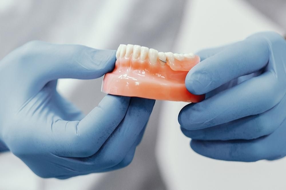 A Person Wearing Blue Gloves Is Holding a Denture in Their Hands — Peter McLennan Denture Clinic in Grafton, NSW