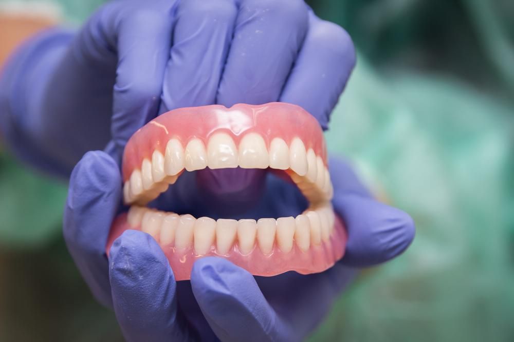 A Person Wearing Purple Gloves Is Holding a Denture in Their Hands — Peter McLennan Denture Clinic in Grafton, NSW