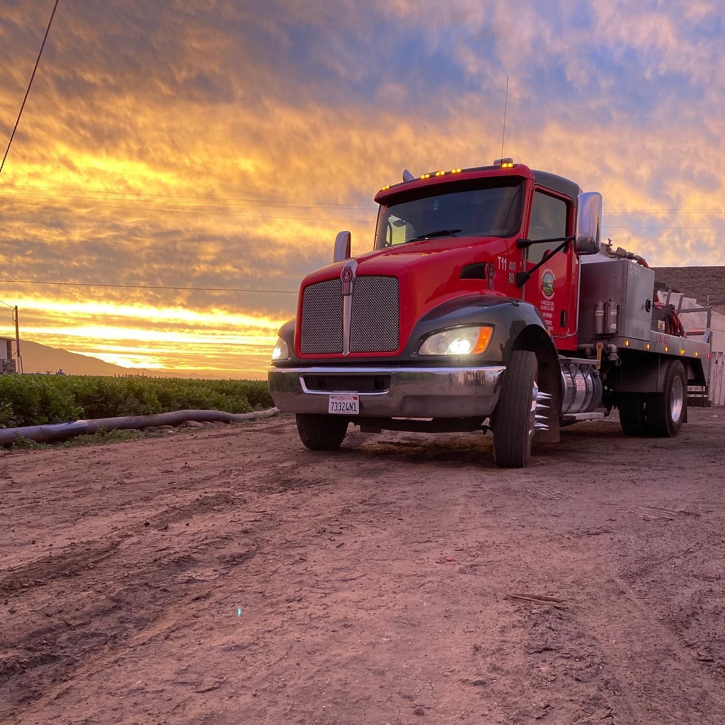A red truck is parked on a dirt road at sunset
