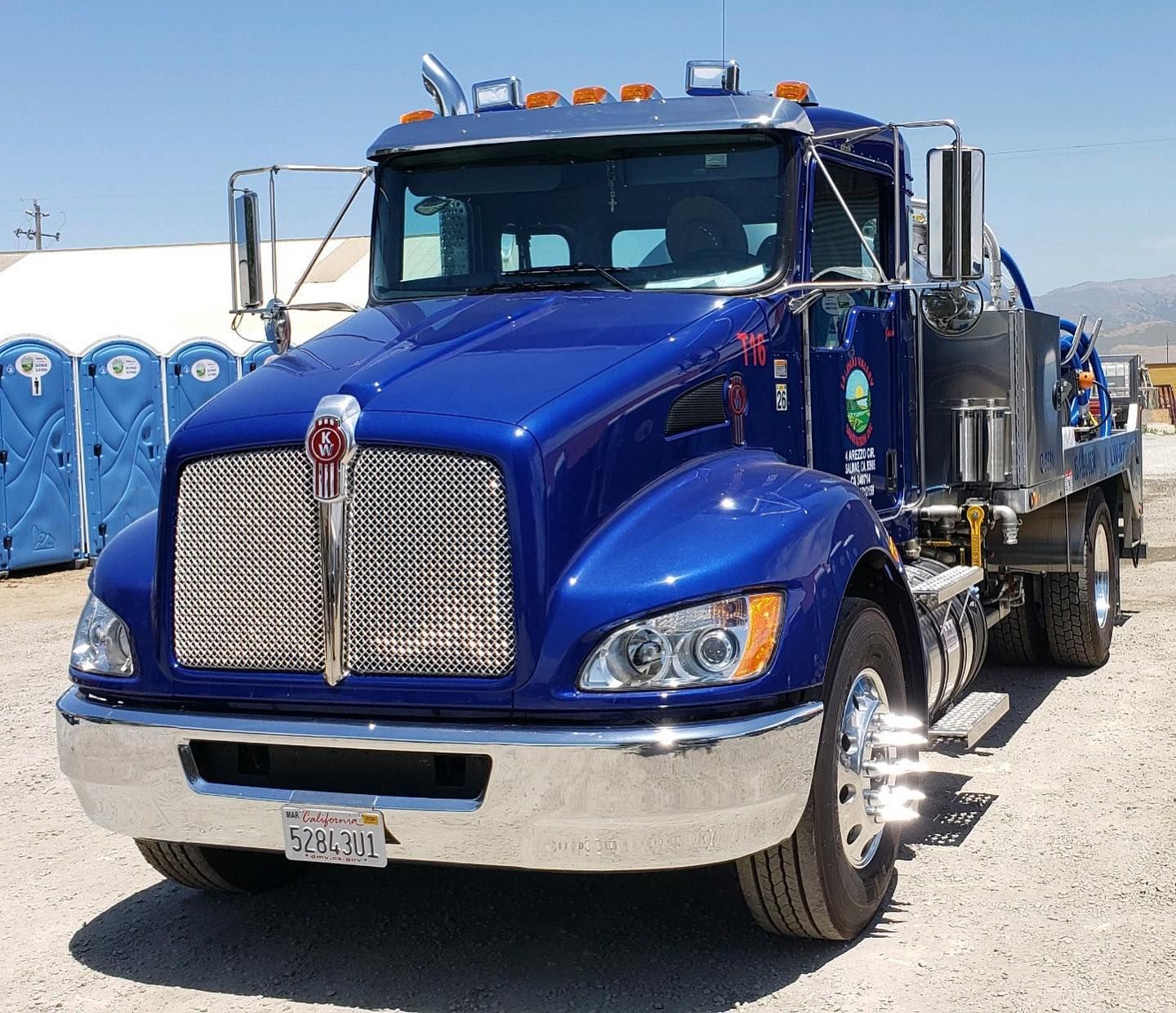 A blue kenworth truck is parked in a dirt lot