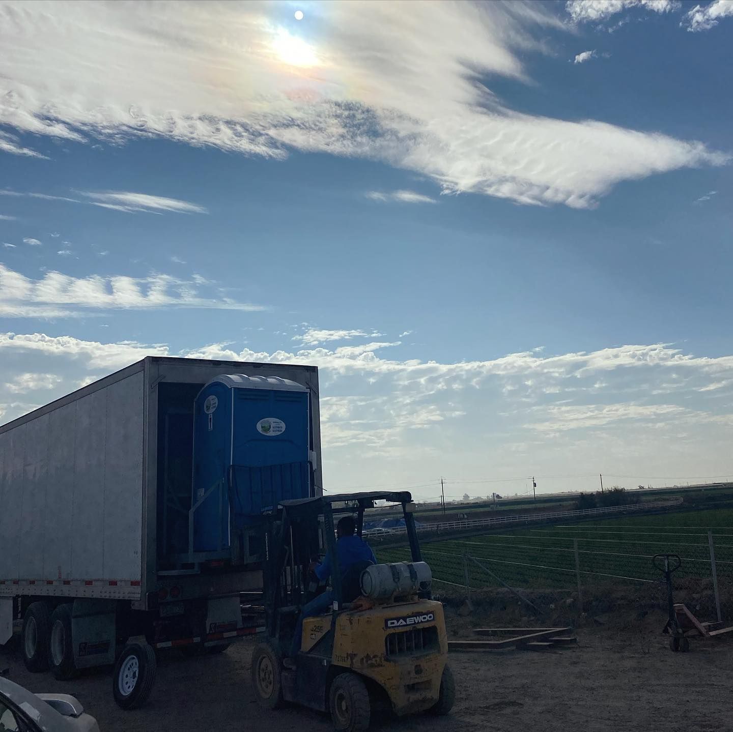 A forklift is loading a portable toilet into a trailer.