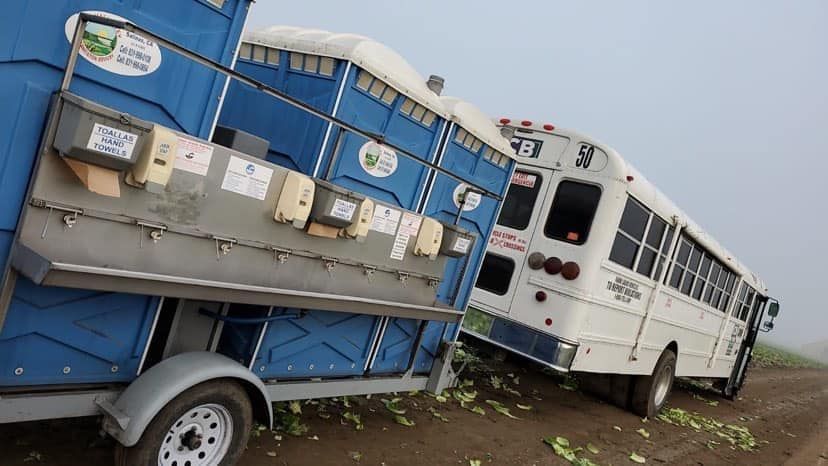 A white bus is parked next to a blue trailer