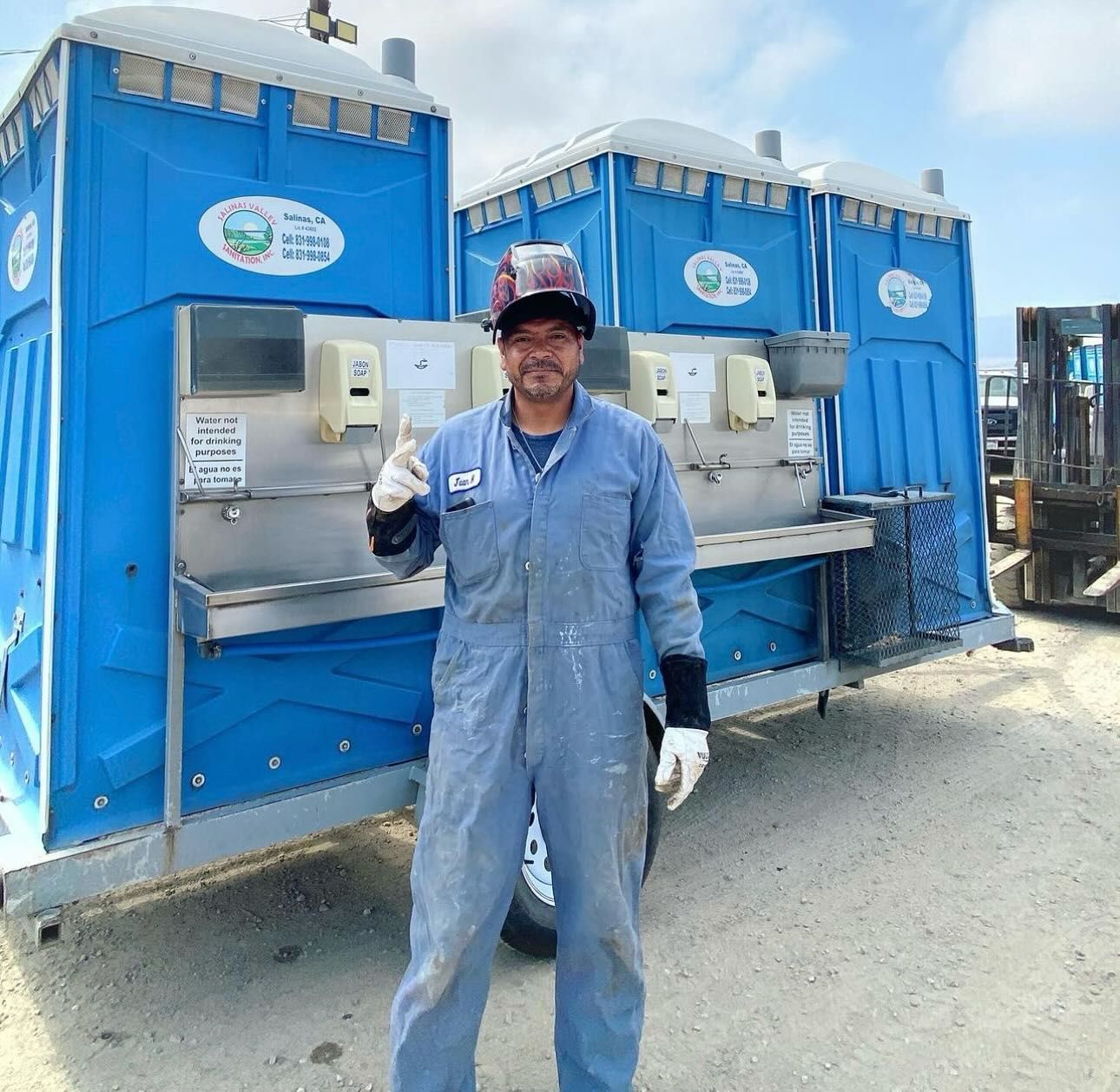 A man in overalls is standing in front of two blue portable toilets